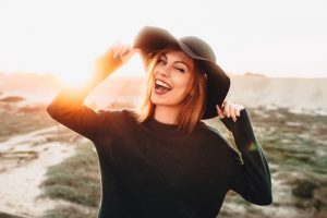 portrait of beautiful blonde young woman in glasses and holding hat and winking on the beach