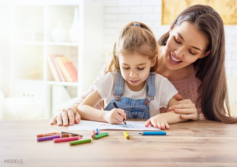 Mother and daughter spending time coloring on paper with colored pencils.