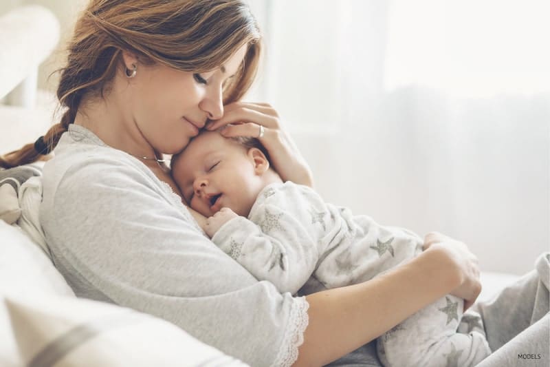 Loving mom carrying her newborn baby at home. Bright portrait of happy mom holding sleeping infant child.