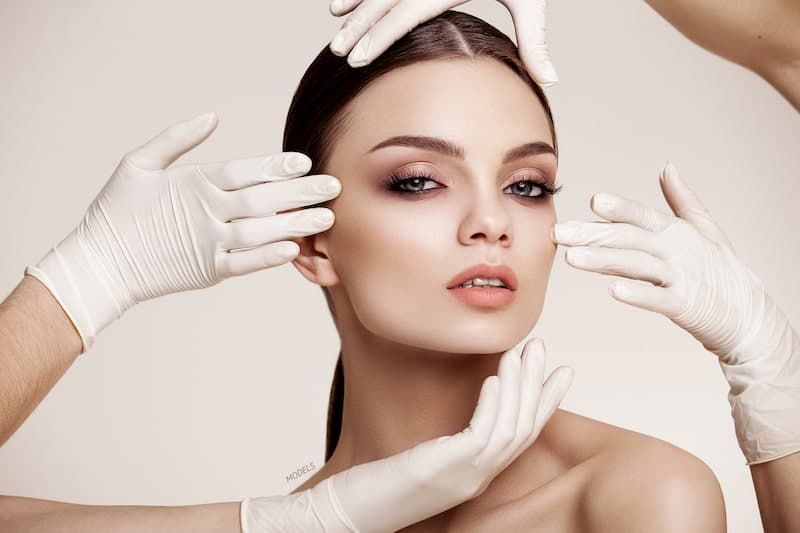 Young woman with surgical-gloved hands surrounding her face.