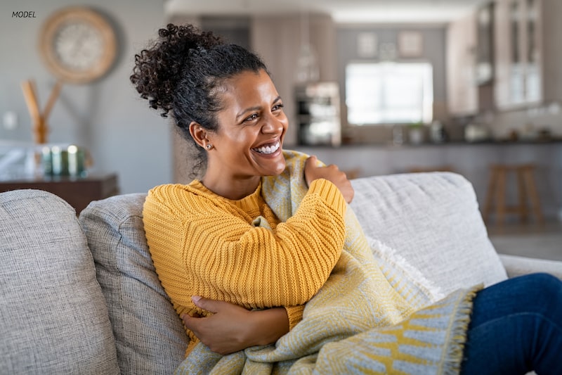 Woman sitting on couch, wrapped in a sweater and blanket.