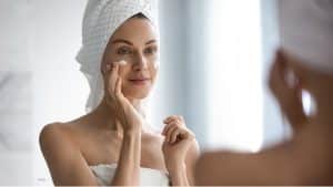 Woman with hair wrapped in white towel putting on skin cream.