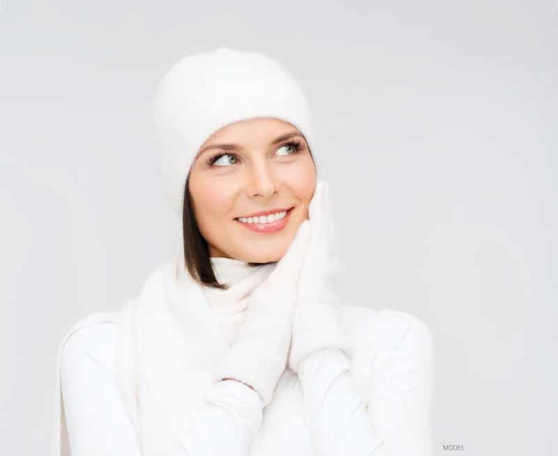 Woman with perfect skin dressed in a white sweater, gloves, and hat.