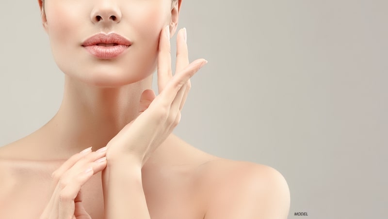 Close up image of a beautiful woman's face, shoulder, and lifted hand with smooth and blemish-free skin