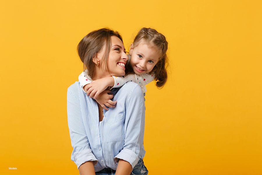 Young mother is embraced by her toddler against a yellow background